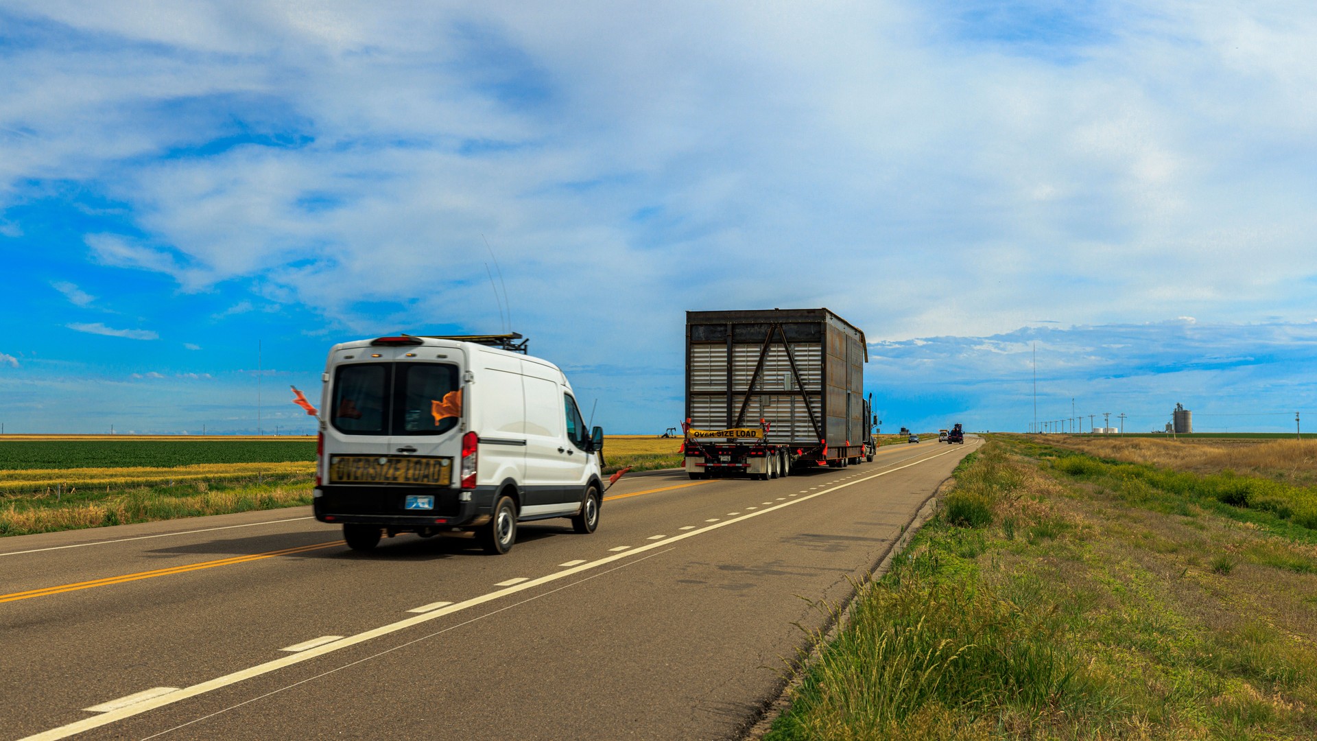Oversize load. Heavy haulage convoy navigates rural landscape. Massive metal structure transported on Kansas highway with escort.